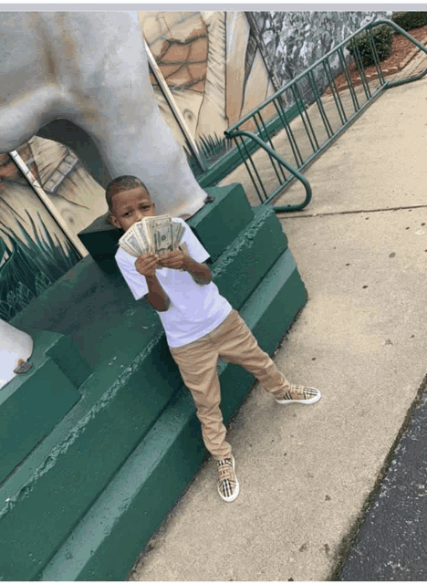 a young boy holding a bunch of money in front of a statue of a horse