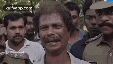 a man with a mustache is standing in a crowd of people and talking to a police officer .