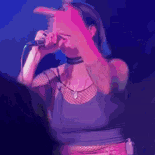 a woman is singing into a microphone and covering her face with her hand