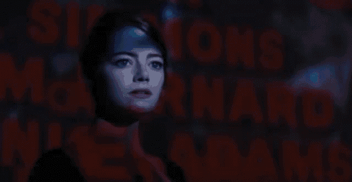 a woman is standing in front of a projection of a man 's face in a dark room .