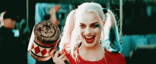 a woman in a harley quinn costume is smiling and holding a drum with a smiley face on it .