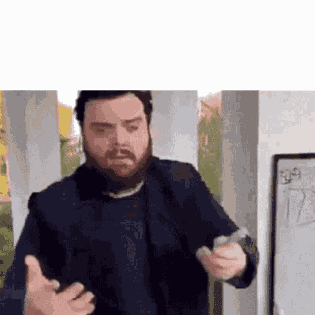 a man with a beard is standing in front of a whiteboard and holding a piece of paper .