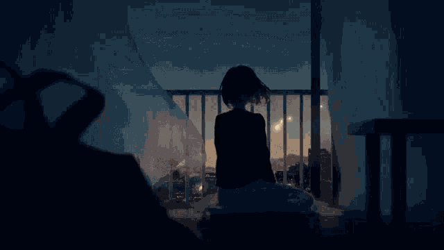 a girl sits on a balcony looking out at the city at night
