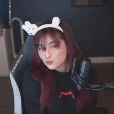 a woman wearing a headband with bunny ears is sitting in front of a microphone and making a funny face .