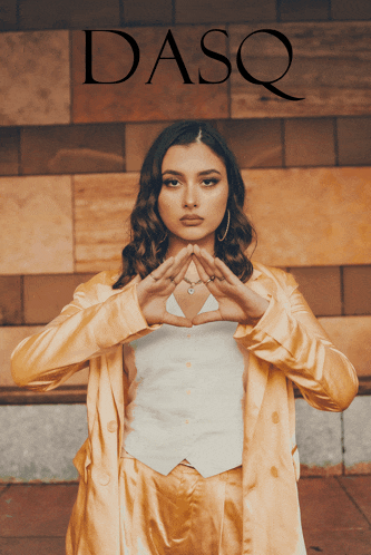 a woman making a heart shape with her hands in front of a dasq sign