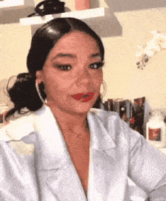 a woman wearing a white shirt and red lipstick is sitting in front of a shelf .