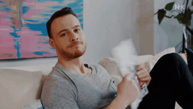 a man is sitting on a couch with a hk logo in the background