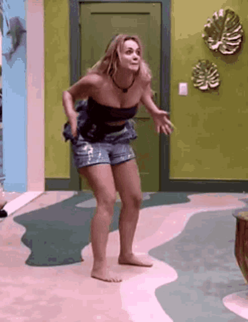 a woman in a strapless top and shorts is dancing on a rug in a room .