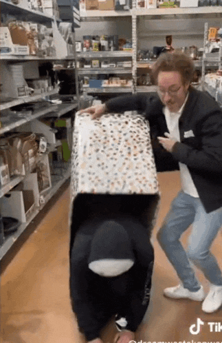 a man is pushing a person in a box in a store while another man looks on .