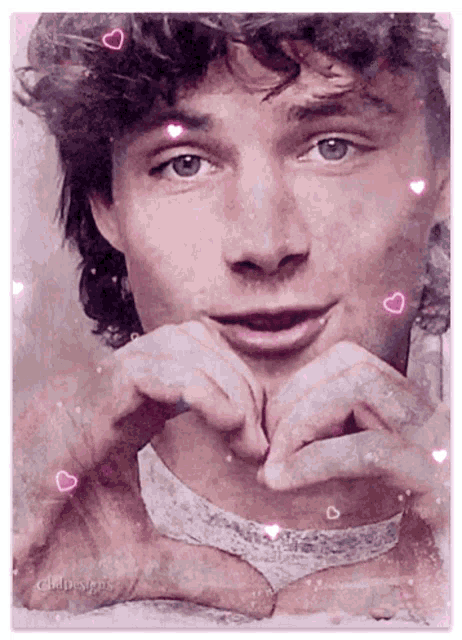 a man making a heart shape with his hands with pink hearts around him