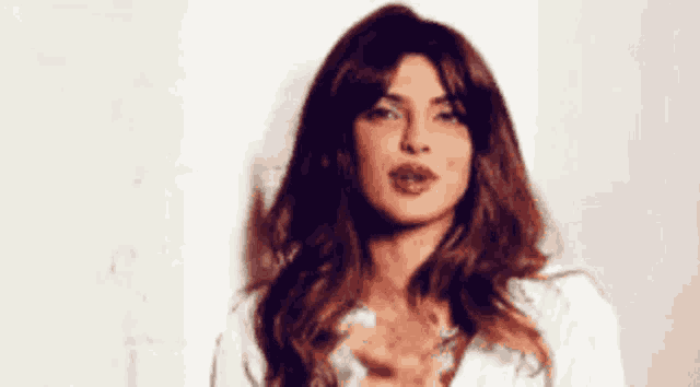 a woman with long brown hair is wearing a white shirt and making a face .