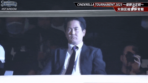 a man in a suit and tie is watching a cinderella tournament in a dark room