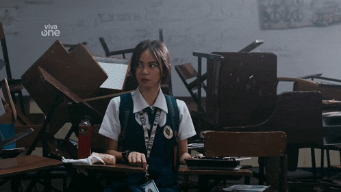 a girl sits at a desk in a classroom with a sign that says viva one on it
