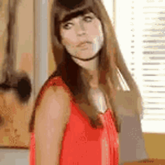 a woman in a red dress is standing in front of a window and making a funny face .