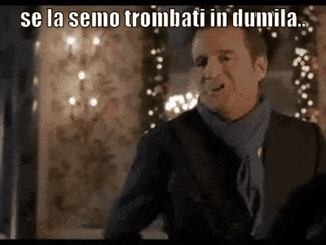 a man in a suit and tie is standing in front of a christmas tree and says se la semo trombati in dumila