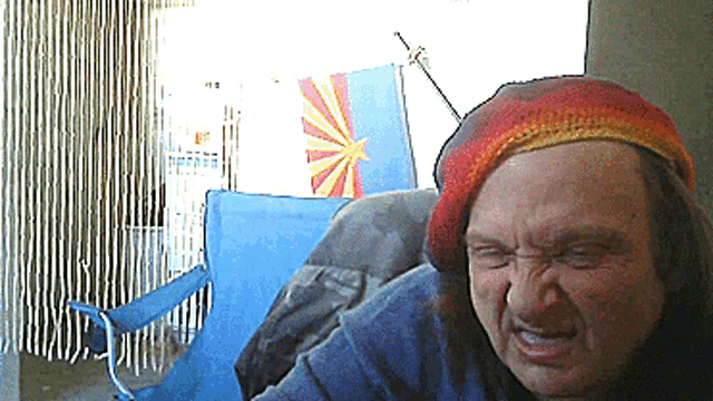 a man wearing a rainbow colored hat is sitting in front of a flag of arizona