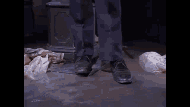 a man 's feet are standing on a dirty floor next to a pile of trash