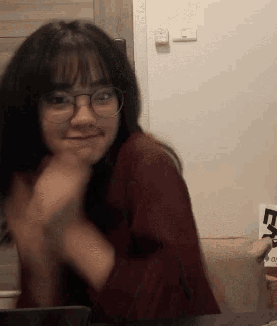 a girl wearing glasses and a maroon sweater is sitting at a table