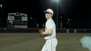 a baseball player stands in front of a scoreboard that says claude m smith field