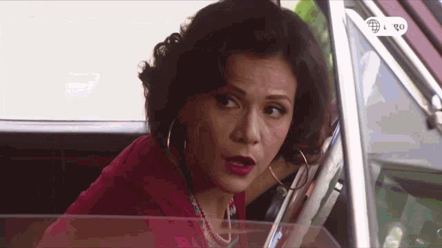 a woman in a red shirt is sitting in a car with the number 90 on the screen