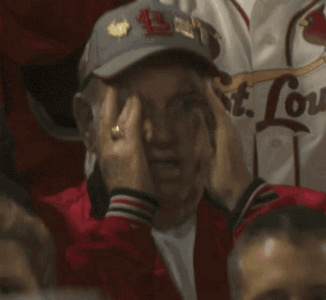a man wearing a louis cardinals hat covers his face with his hands