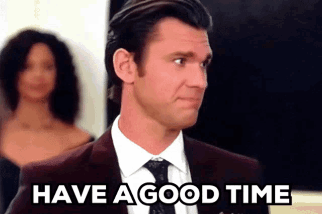 a man in a suit and tie is saying `` have a good time '' while standing in front of a woman .