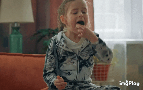 a little girl is sitting on a couch eating a chocolate bar .