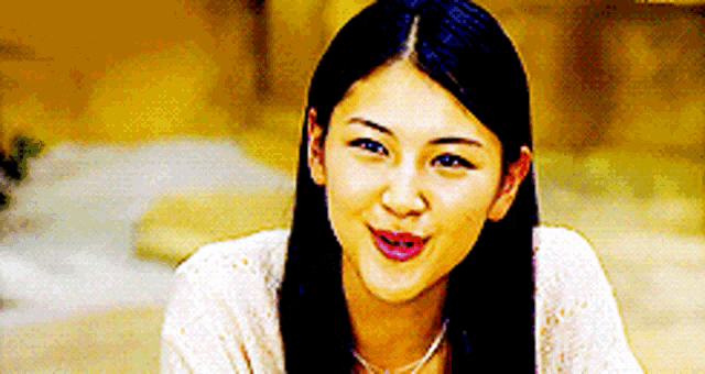 a woman with long black hair is smiling and wearing a white sweater and a necklace