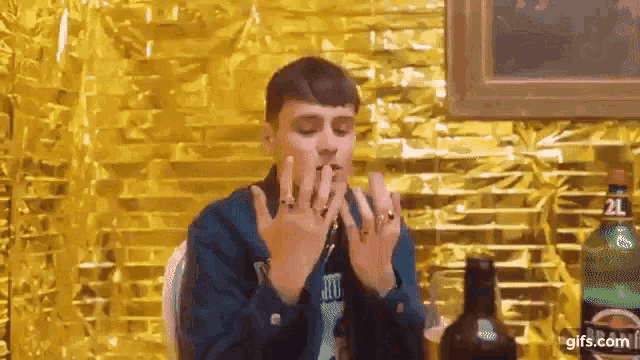 a man is sitting at a table with a bottle of alcohol in front of a gold background .