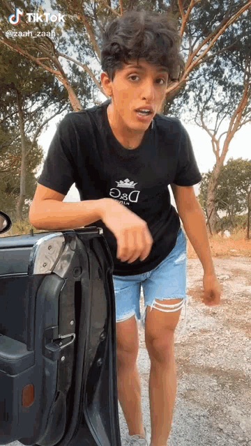 a young man is standing next to a car wearing a black t-shirt that says d & d