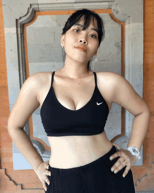 a woman wearing a black nike sports bra stands in front of a stone wall