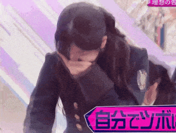 a woman covering her mouth in front of a sign that says ' 自分 で ツボ ' on it