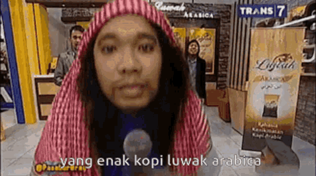 a man wearing a turban and a hat is talking into a microphone on a television show .