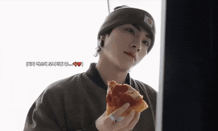 a young man wearing a beanie is eating a large slice of pizza .