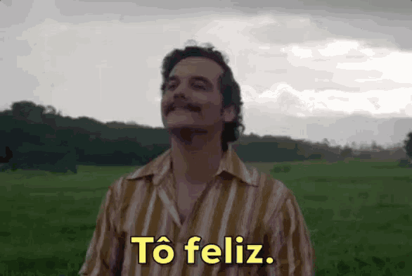 a man in a striped shirt is standing in a field and saying to feliz