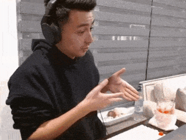 a man wearing headphones is sitting at a table with his hands out .
