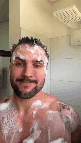a man with a tattoo on his arm is taking a shower with soap on his face