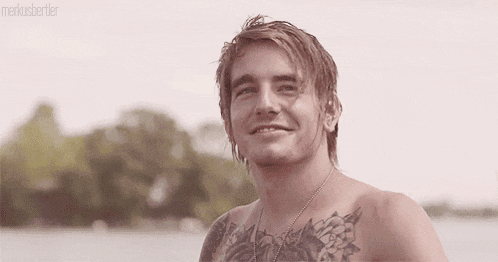 a shirtless man with a tattoo on his chest is smiling and pointing