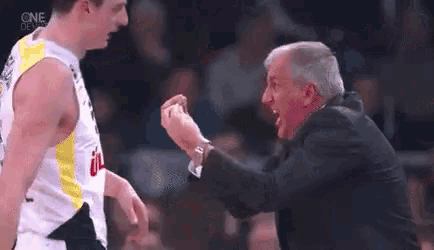 a man in a suit is talking to a basketball player on a basketball court .