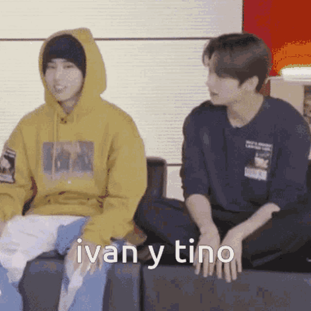 two young men are sitting on a couch and one of them is wearing a yellow hoodie