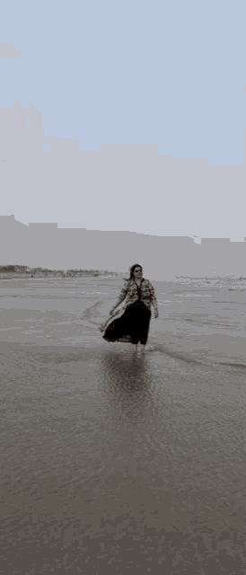 a woman in a plaid shirt and black skirt is walking on the beach