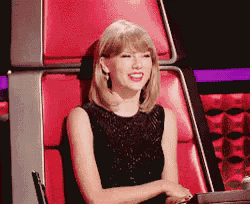a woman in a black dress is sitting in a red chair laughing .