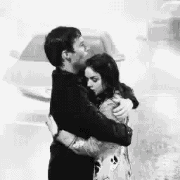 a man and a woman are hugging in the rain in a black and white photo .