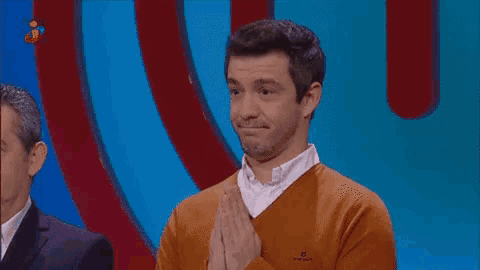 a man in an orange sweater is clapping in front of a blue background with the word sorpresa on it
