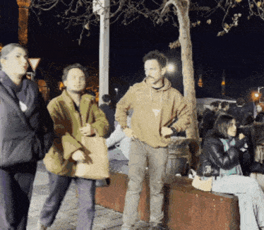 a man wearing a brown sweatshirt with a t on it stands in front of a group of people