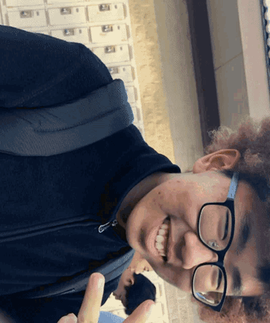 a young man wearing glasses is smiling and giving a middle finger