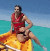a man in a red life jacket is sitting on a yellow kayak in the ocean