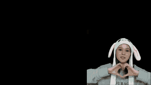 a girl wearing a bunny hat is making a heart with her hands .