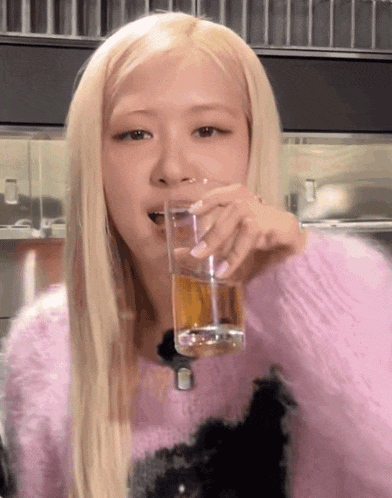 a blonde woman in a pink sweater drinks from a glass