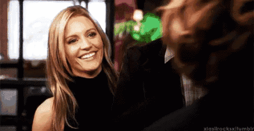 a woman in a black top is smiling at a man in a suit in a restaurant .